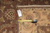 Load image into Gallery viewer, A close-up of an ornate patterned area rug with a beige central field, brown borders, and floral motifs in muted red, blue, and green tones. A yellow tape measure and a small white tag are placed on the rug to indicate scale and product details.