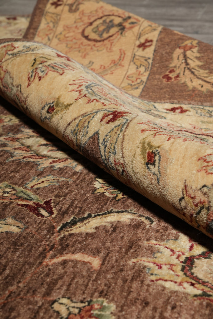 A close-up of a traditional patterned area rug, partially rolled to show its beige and brown floral design with red and green accents.