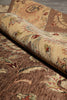 Load image into Gallery viewer, A close-up of a traditional patterned area rug, partially rolled to show its beige and brown floral design with red and green accents.
