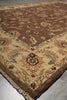 Load image into Gallery viewer, A close-up of a traditional patterned area rug with a cream and brown base, featuring floral motifs and a fringed edge, shown on a gray tiled floor.