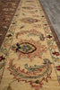 Load image into Gallery viewer, A close-up view of a long area rug runner with an ornate traditional pattern in beige, rust red, and muted blue on a dark brown base.