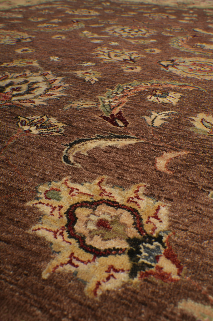 Close-up of a traditional patterned rug in warm brown tones with cream, red, and muted blue floral motifs.