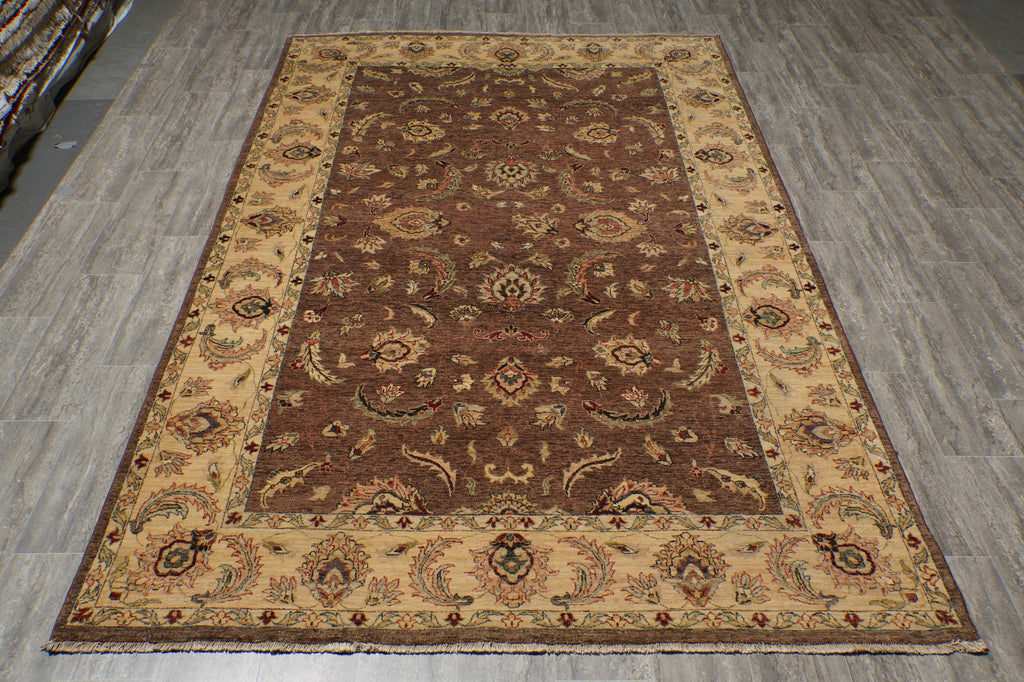 A rectangular area rug with an ornate traditional pattern, featuring a dark brown center field, a beige border, and accents of red and green.