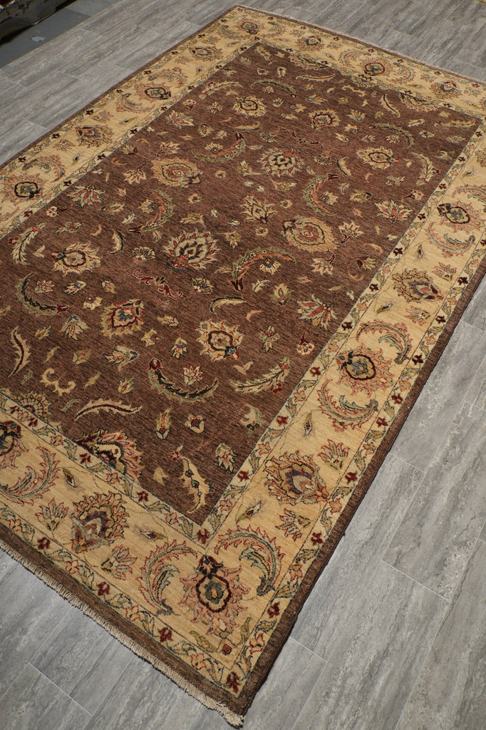 A traditional oriental area rug with a brown center and beige borders, laid out on a gray wood-look floor.