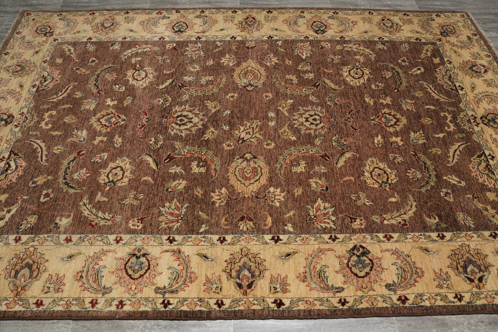 A traditional oriental area rug with a warm brown center field, detailed floral and medallion motifs, and a beige border with multicolor accents, laid out on a gray tiled floor.