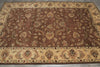 Load image into Gallery viewer, A traditional oriental area rug with a warm brown center field, detailed floral and medallion motifs, and a beige border with multicolor accents, laid out on a gray tiled floor.