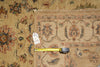 Load image into Gallery viewer, A close-up of a traditional patterned rug with a beige base and muted red, blue, and green floral motifs, shown with a yellow tape measure and a white tag on the floor.