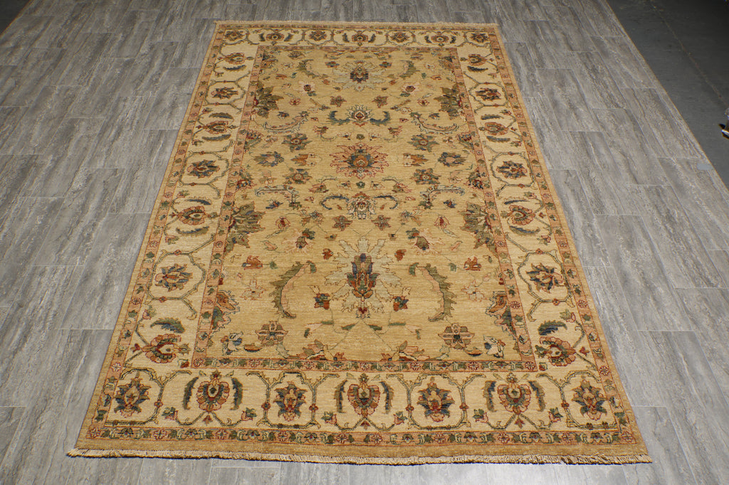 A rectangular vintage-style area rug with an ornate floral pattern, laid out on a gray wood-look floor. The rug features a warm beige base with brown, blue, and rust-red accents in its detailed motifs.