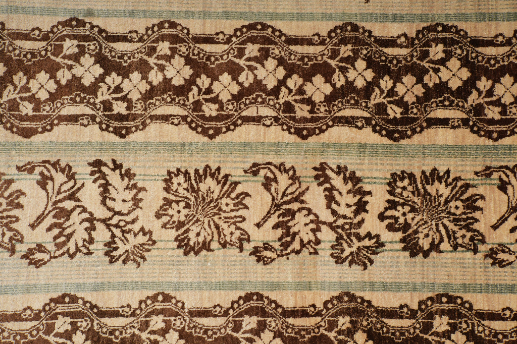 A close-up of a woven textile pattern featuring dark brown floral and lace-like horizontal bands over a beige and muted blue striped background.