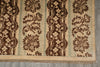 Load image into Gallery viewer, A close-up of a patterned area rug with vertical stripes featuring dark brown floral and ornamental motifs on a beige background, with a fringed edge, laid on a gray floor.
