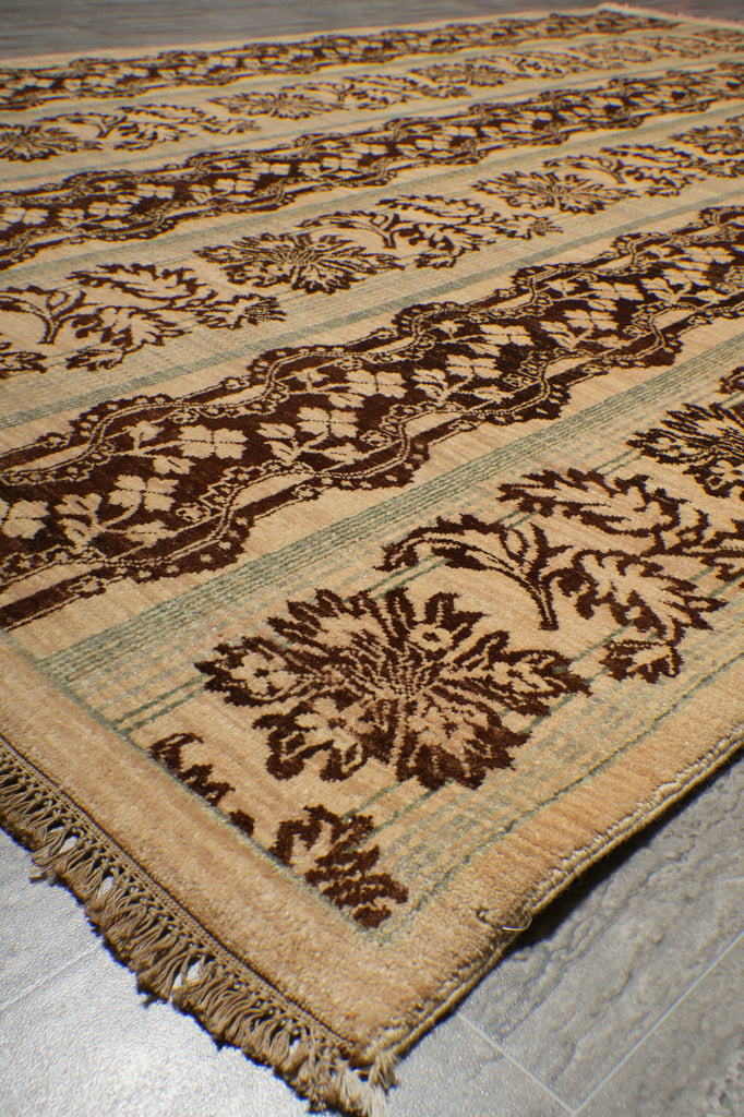A close-up of a patterned area rug with a beige base, dark brown floral motifs, and a light green stripe border, shown on a gray tiled floor.