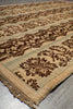 Load image into Gallery viewer, A close-up of a patterned area rug with a beige base, dark brown floral motifs, and a light green stripe border, shown on a gray tiled floor.