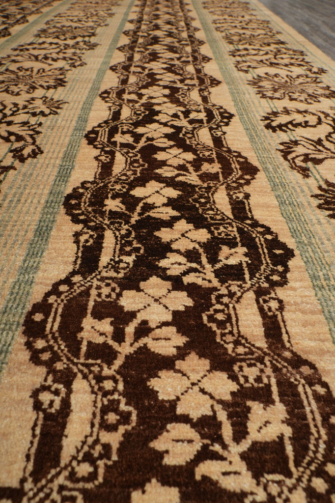 Close-up of a woven rug showing a dark brown ornate floral border pattern on a beige background with muted green stripes.