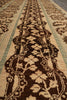 Load image into Gallery viewer, Close-up of a woven rug showing a dark brown ornate floral border pattern on a beige background with muted green stripes.