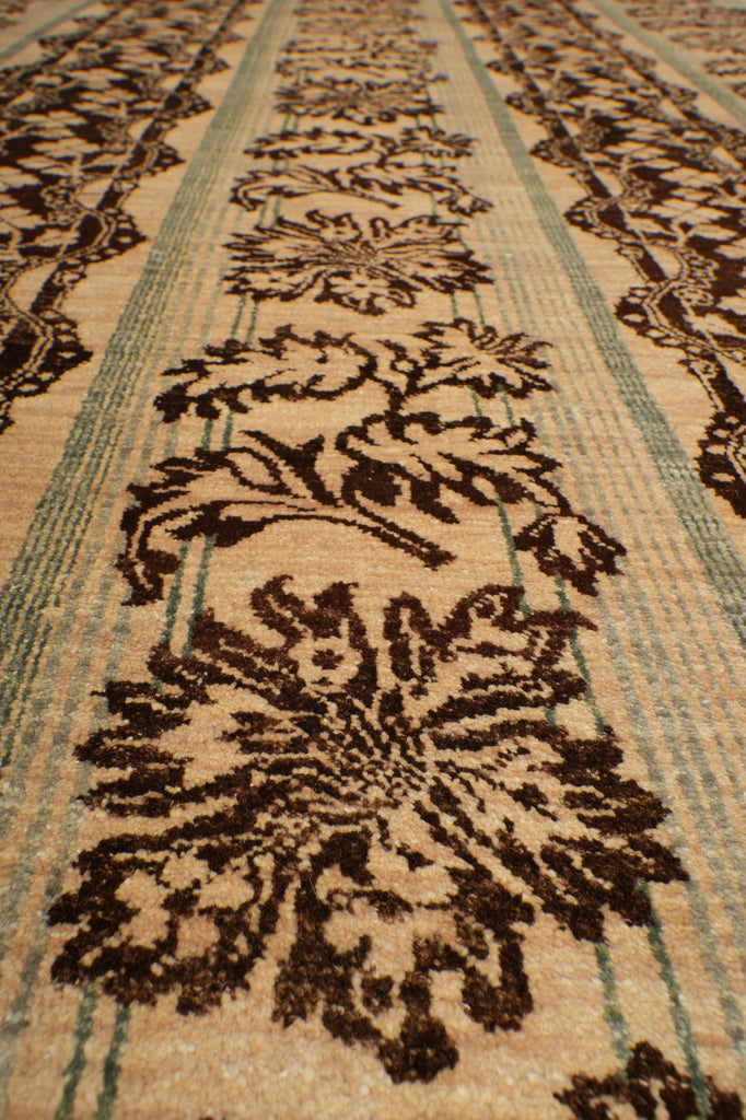 Close-up of a woven rug or textile with a repeating floral pattern in dark brown on a warm beige background, with thin muted green stripes running horizontally.