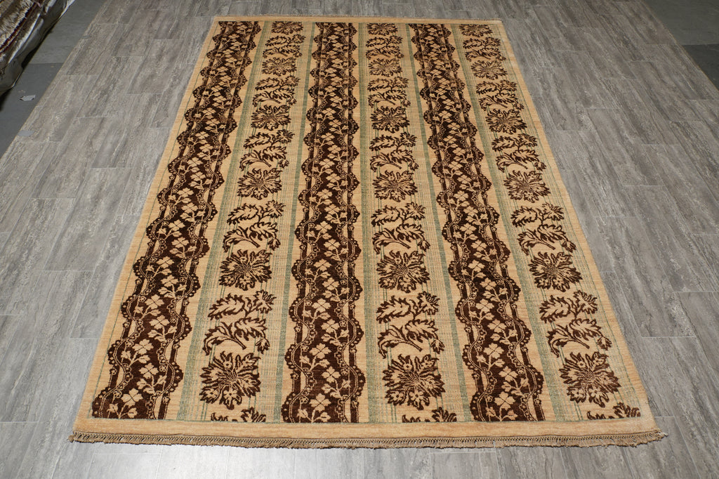 A rectangular area rug with a traditional floral pattern in vertical stripes, featuring a beige base with dark brown and black motifs, shown on a gray wood-look floor.