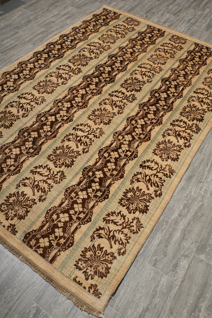 A rectangular area rug with a traditional floral pattern, shown at an angle on a gray wood-look floor. The rug features alternating vertical stripes of dark brown floral motifs, beige bands, and light sage green stripes.