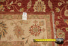 Load image into Gallery viewer, A close-up of a patterned area rug with a red outer field, beige inner field, and floral motifs. A yellow tape measure is placed along the fringe to show the rug's width, and a small product tag is attached near the center.