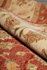 Load image into Gallery viewer, A close-up of a rolled area rug showing its detailed floral and geometric patterns in warm rust red, cream, and olive green tones.