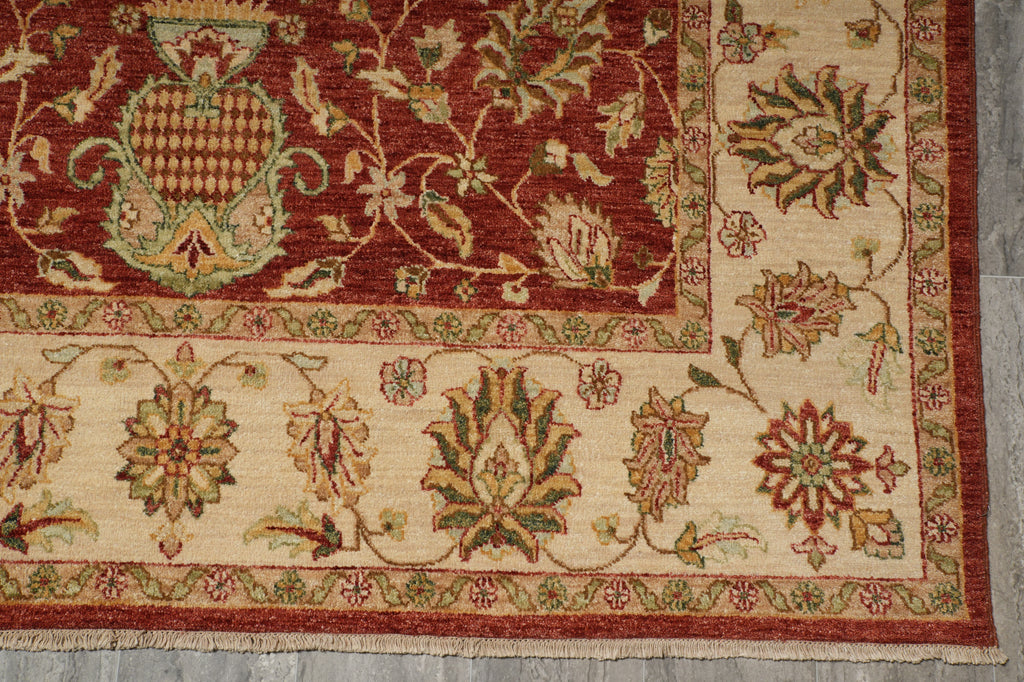 A close-up of a traditional patterned rug showing a deep red field with a large central medallion and a cream border decorated with floral motifs in red, green, and beige.