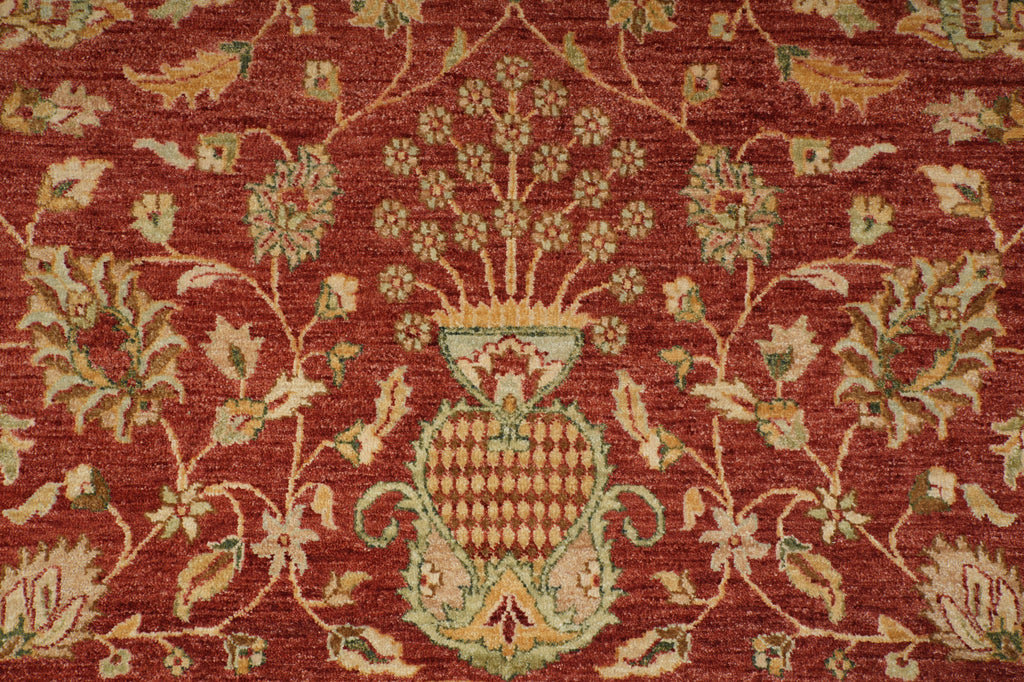 A close-up of a traditional patterned rug featuring a deep red background with beige, green, and gold floral motifs and a central decorative medallion.