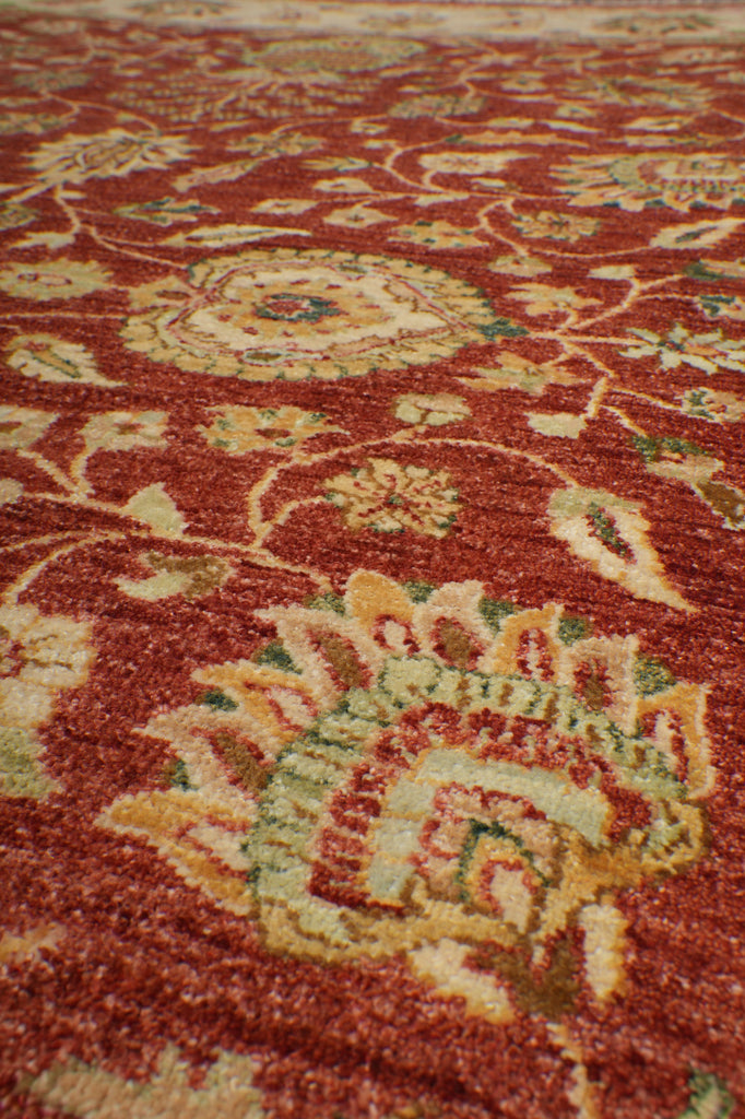 Close-up of a traditional patterned rug with a warm rust-red background and cream, beige, and muted green floral motifs.