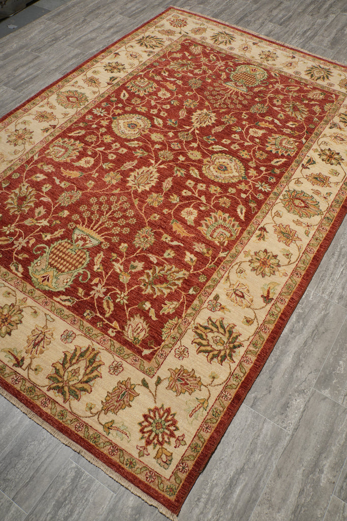 A traditional oriental area rug with a deep red central field and a beige border, displayed on a gray wood-look floor.