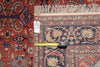 Load image into Gallery viewer, A close-up of a patterned area rug with a red, navy, and beige floral design, showing a fringed edge and a yellow tape measure placed horizontally across the center.