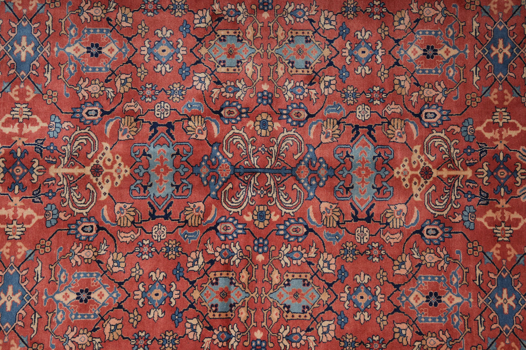 A close-up of a traditional patterned rug with a warm red-orange field, blue and beige medallions, and intricate floral motifs.
