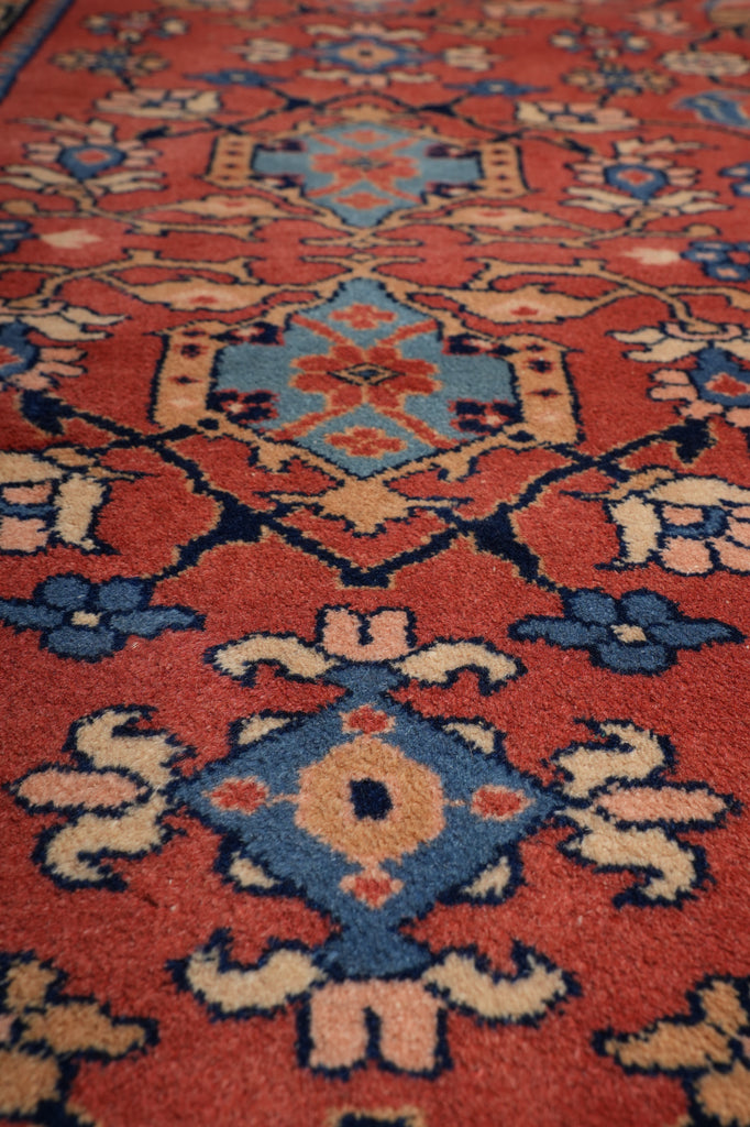 Close-up of a patterned rug with a red-orange field and blue, beige, and cream geometric floral motifs.