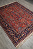 Load image into Gallery viewer, A traditional Persian-style area rug with a red field, navy blue borders, and beige and blue floral motifs, shown laid out on a gray tiled floor.