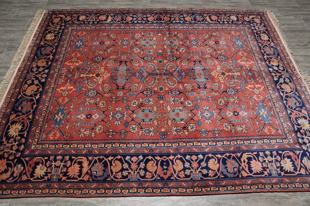 A traditional Persian-style area rug with a vibrant red field, detailed floral motifs, and a dark navy blue border, laid out on a gray tiled floor.