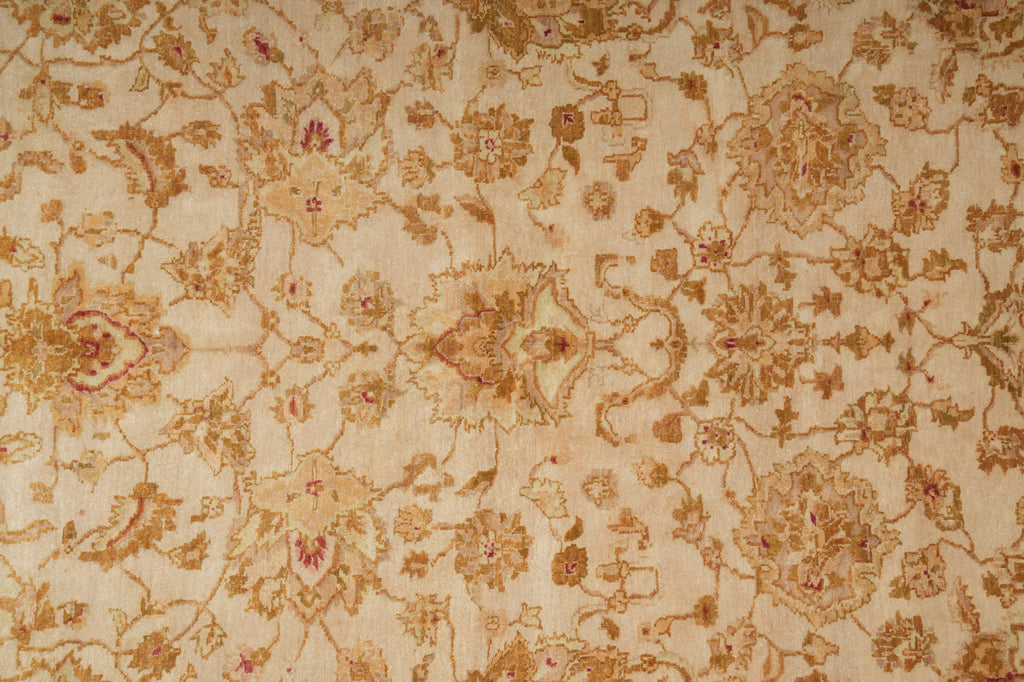 A close-up of a beige fabric with an intricate floral and vine pattern woven in gold, brown, and muted pink threads.