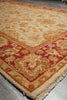Load image into Gallery viewer, A close-up of a patterned area rug corner showing cream, rust red, and gold floral motifs with fringed edges.