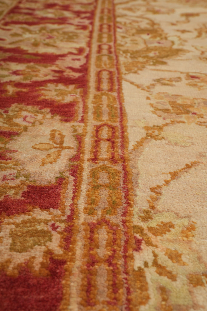 Close-up of an ornate area rug with a central vertical border featuring repeating medallion motifs in rust red, gold, and cream, with a floral field on the right side.