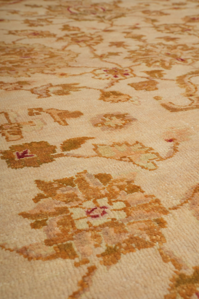 Close-up of a woven rug or textile with an ornate floral pattern in warm beige, tan, brown, and muted pink tones.