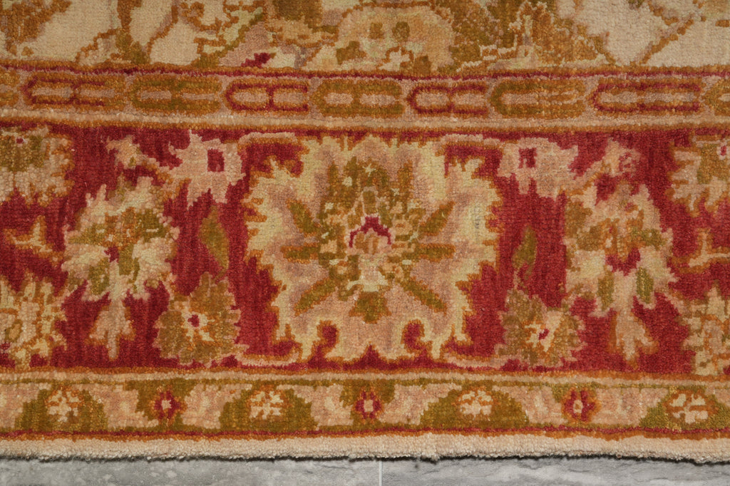 A close-up of a patterned rug showing a traditional floral medallion design in red, beige, and olive green tones.