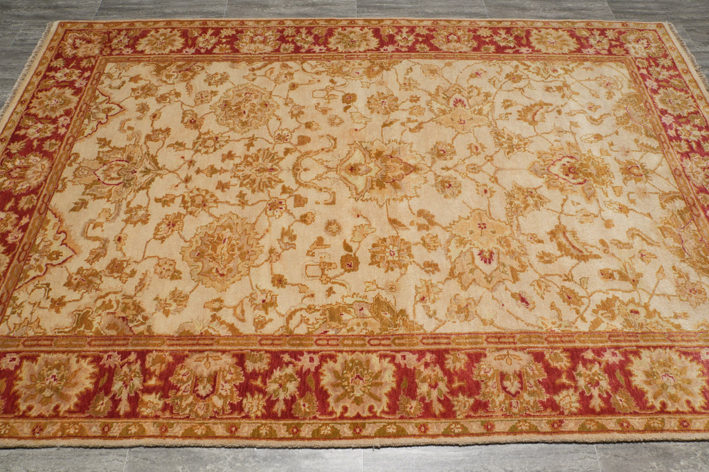 A rectangular area rug with an ornate floral and vine pattern, featuring a cream center field and deep red borders.