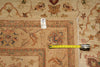 Load image into Gallery viewer, A close-up of a patterned area rug in beige with floral and geometric motifs in muted red, blue, and green, shown with a yellow tape measure and a small white tag.