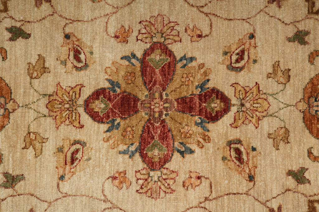 Close-up of a woven rug with a central floral medallion in rust red, beige, ochre, and muted blue-green tones on a warm cream background.