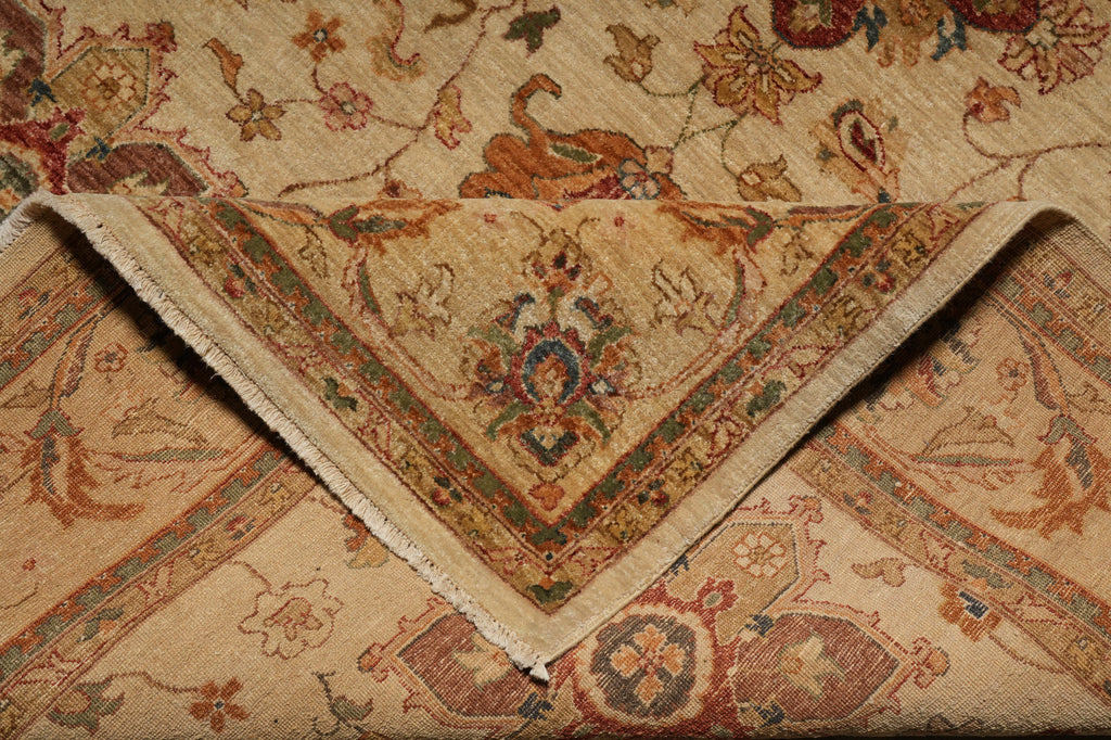 A close-up of a traditional oriental rug with a folded corner showing its beige fringed edge and detailed floral motifs in muted red, green, and blue tones.