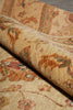 Load image into Gallery viewer, A close-up of a rolled section of a traditional patterned rug showing its beige base with brown, red, and green floral motifs.