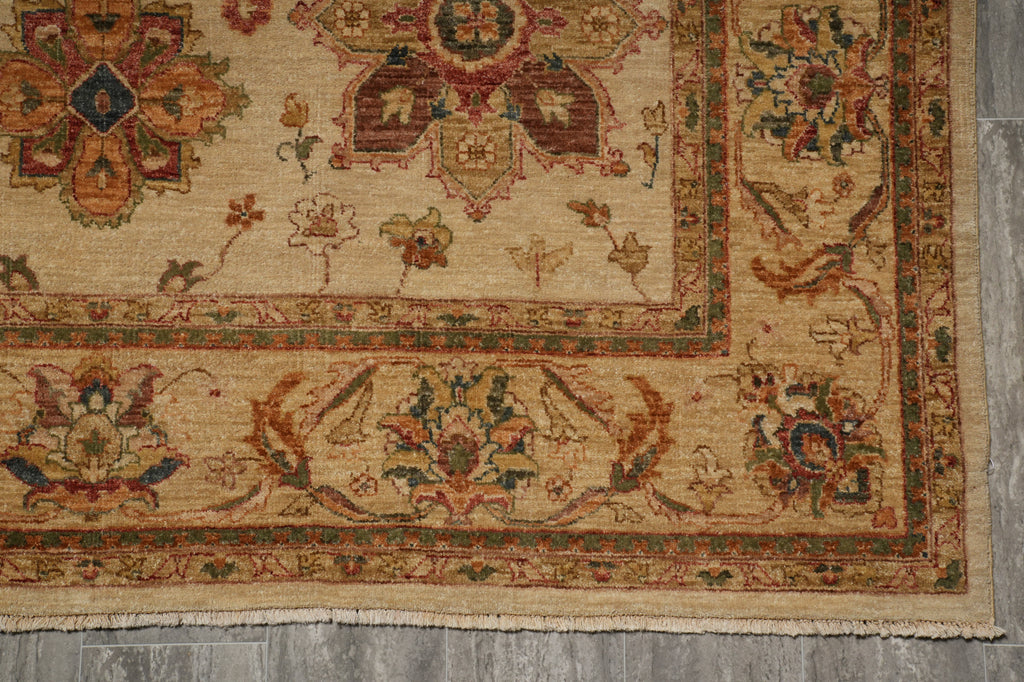 A close-up of a traditional patterned rug showing its beige base with intricate floral and geometric motifs in red, green, and blue, laid out on a gray wood floor.