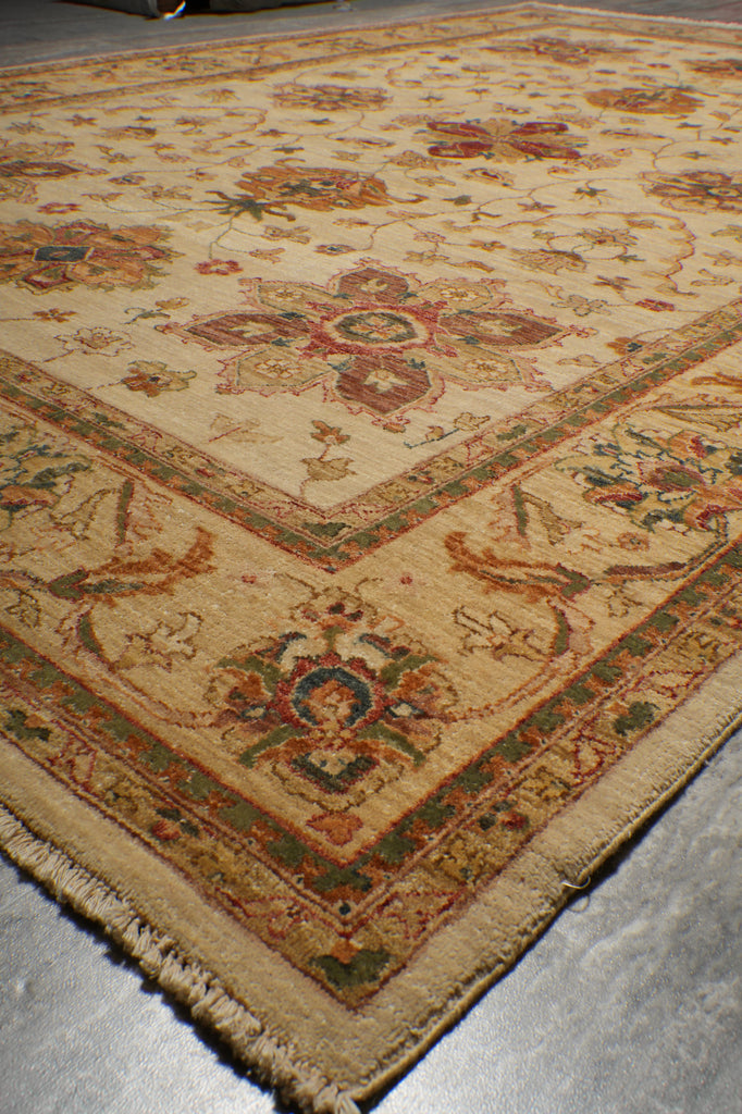 A close-up view of a traditional oriental rug with a beige base and intricate floral patterns in muted red, green, and brown tones, shown on a gray floor.