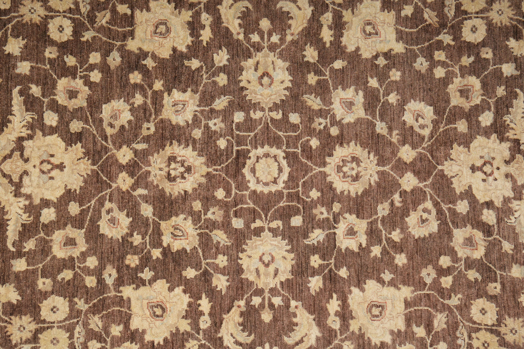 A close-up of a woven rug or textile with an ornate floral and vine pattern in warm beige over a medium brown background.