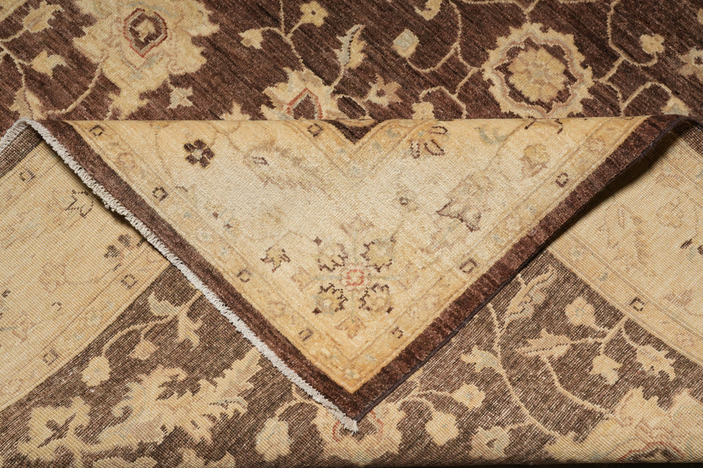 A close-up of a folded area rug showing both its beige and brown sides with traditional floral and vine patterns.
