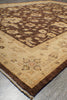 Load image into Gallery viewer, A close-up of a traditional patterned area rug showing its corner and fringe, featuring a dark brown central field with beige floral motifs and a wide beige border on a gray floor.