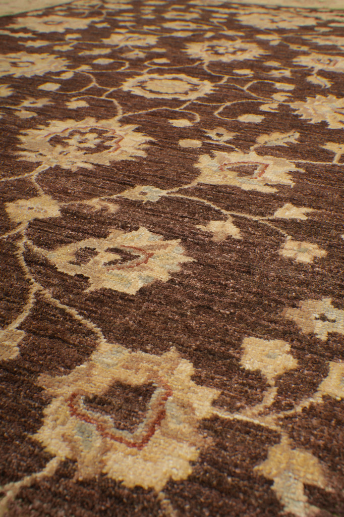 A close-up of a patterned rug or textile with a dark brown base and beige floral motifs.