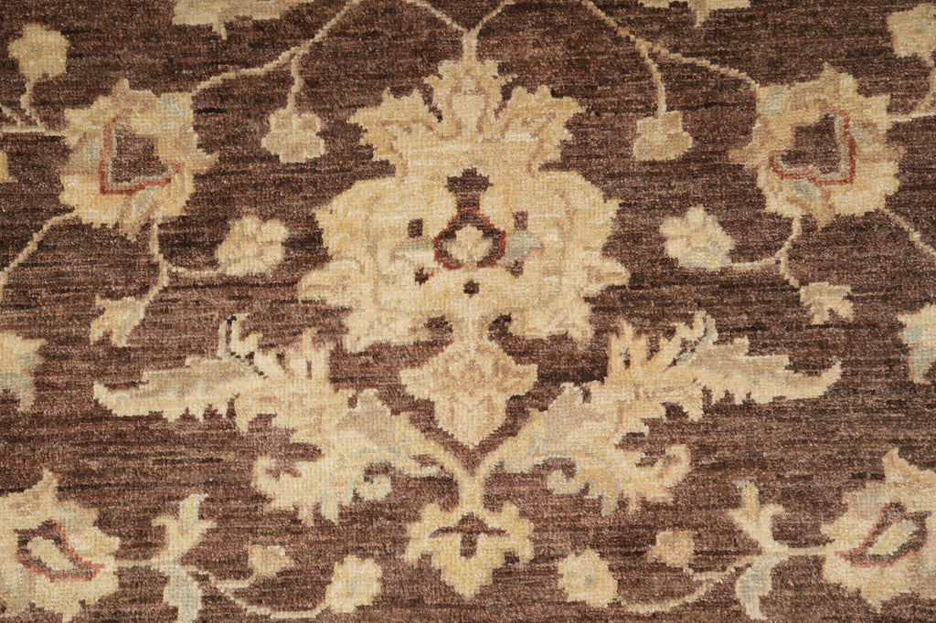 A close-up of a traditional patterned rug featuring a central floral medallion and scrolling vine motifs in cream and light beige on a dark brown background.