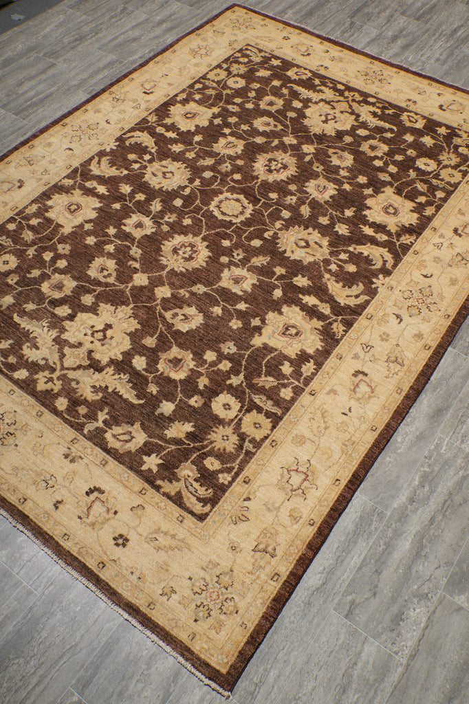 A rectangular area rug with an intricate floral pattern, featuring a dark brown center and a beige border, laid out on a gray wood-look floor.